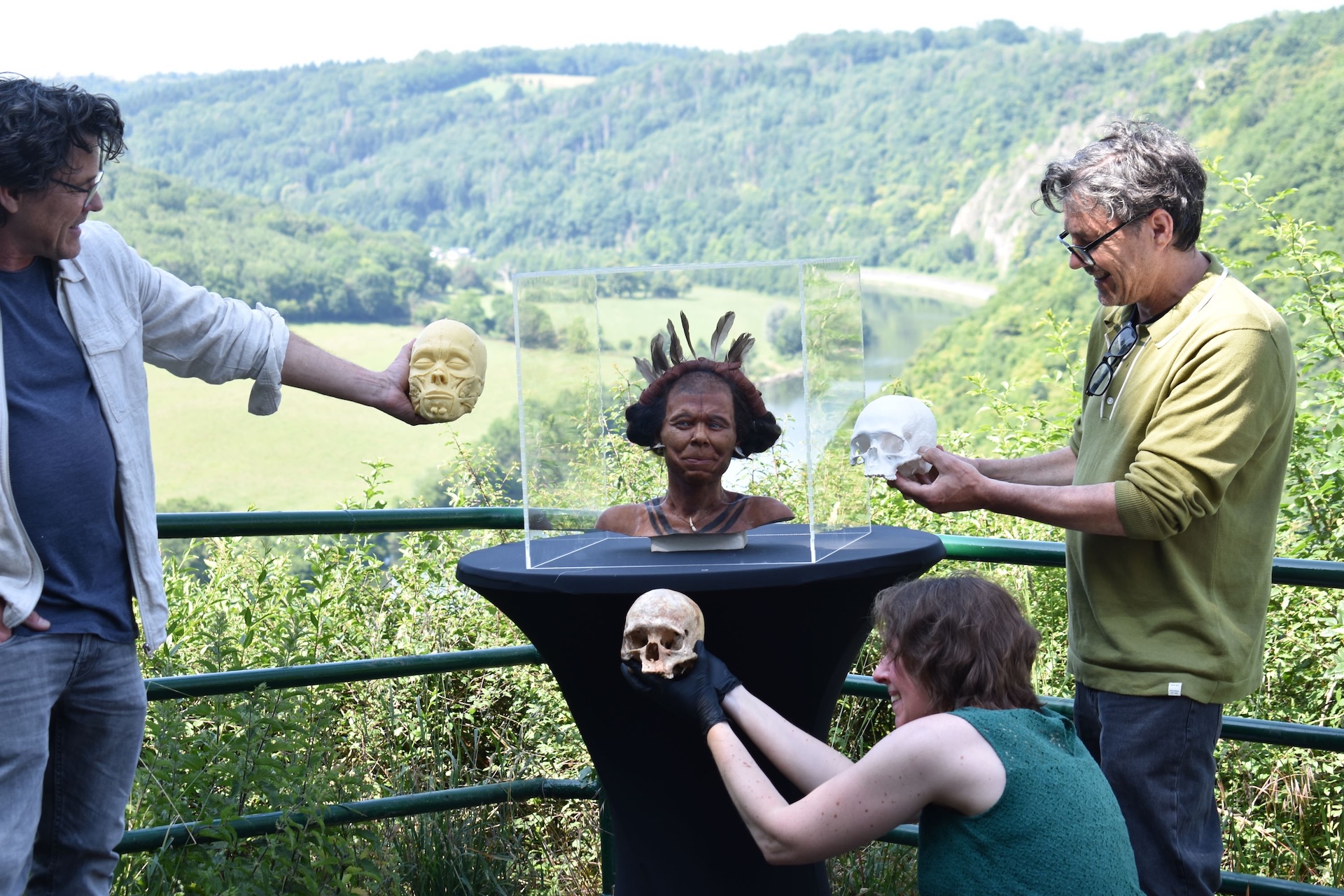 Three people stand around the reconstructed head holding a skull, a model of a skull, and an incomplete model of a head
