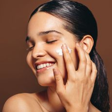 woman applying cream to her cheek with her eyes closed