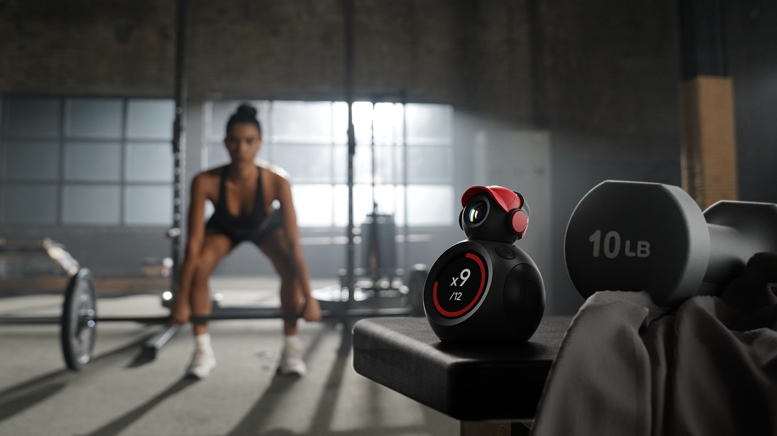 Camera mounted on top of a circular screen, with a person exercising with a barbell in the background
