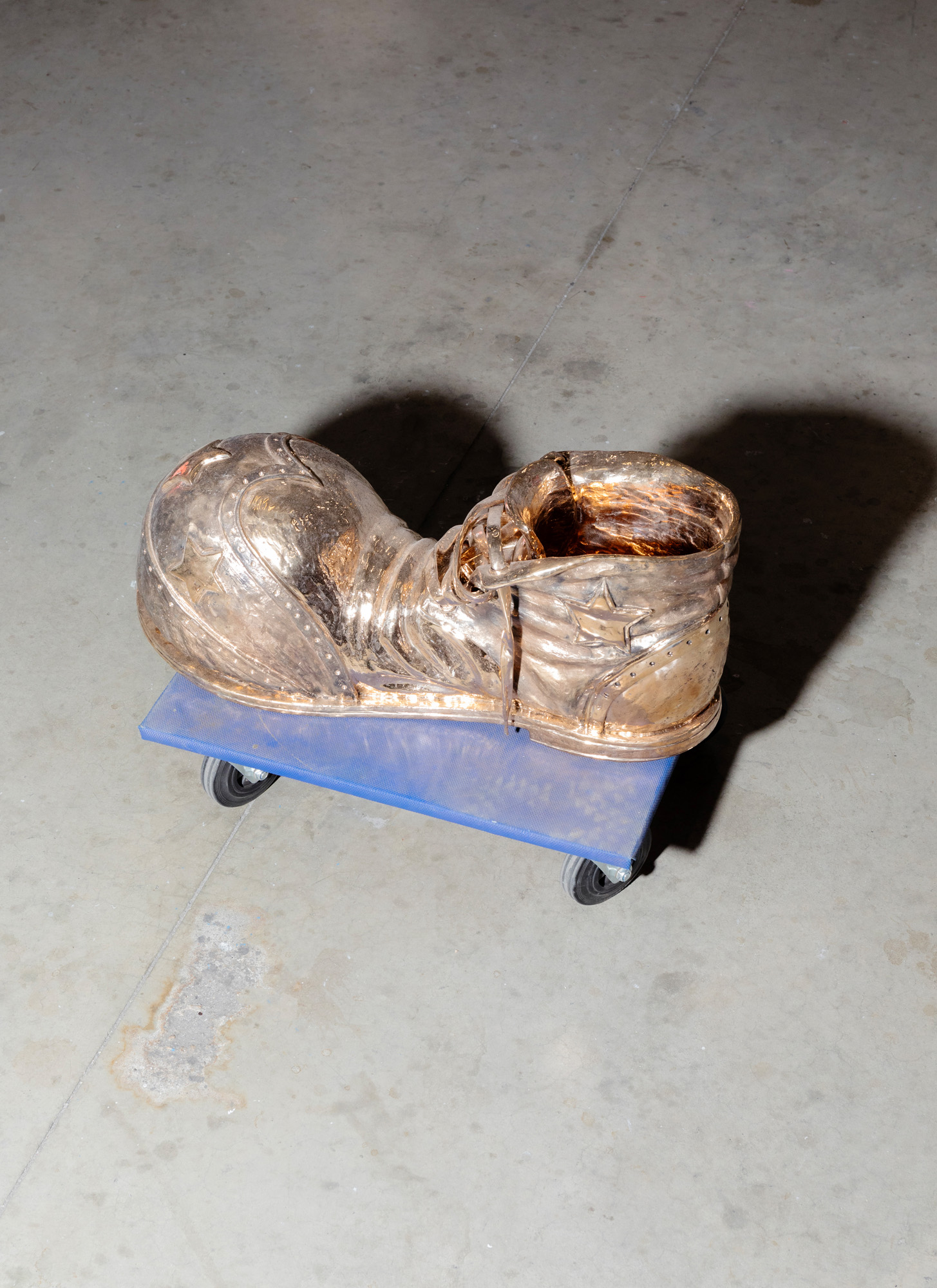 A brass sculpture of a shoe on a blue wheeled platform inside Studio Job&#039;s Tilburg workshop