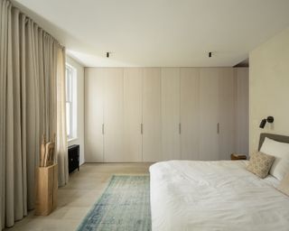 Minimalist bedroom with wooden wardrobe, blue rug and white bed linen