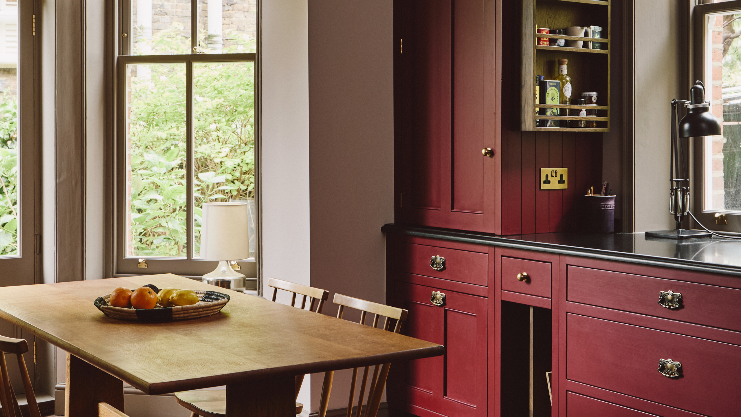Crimson-painted kitchen area with large, rustic windows and a wooden dining set.