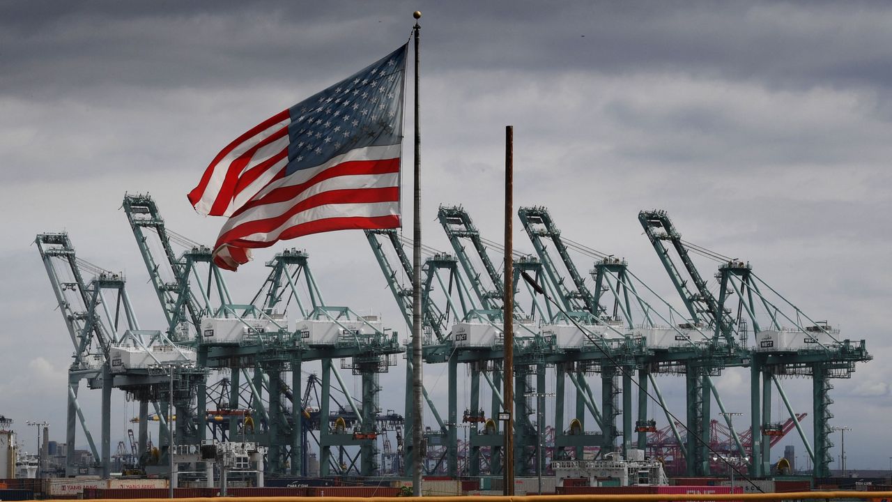 The US flag flies over shipping cranes and containers 