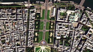 A view looking down from very high at a section of city comprised of buildings and green landscapes.