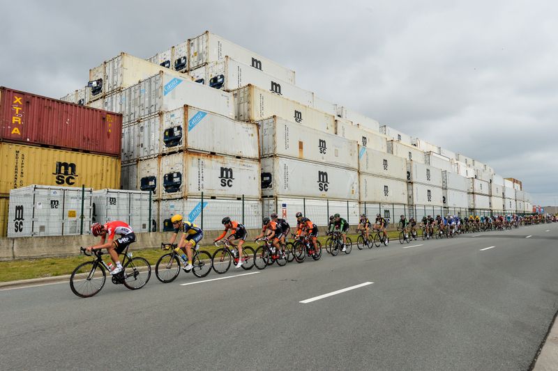 The peloton passes the shipping containers