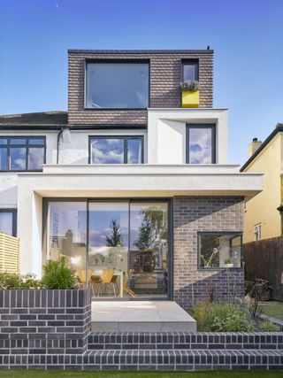 Two storey extension with white render on the rear of a traditional property in London, with grey brick wall in the garden