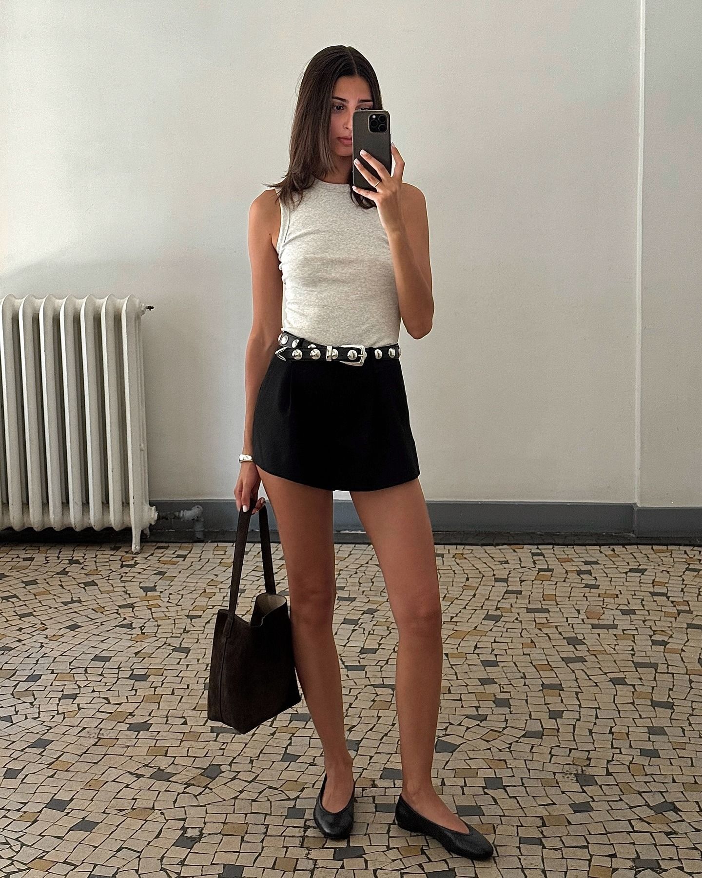 Influencer @salome.mory wears black shorts with a grey tank top. She accessorised with a black studded belt, a dark brown suede bag and black leather ballet flats.