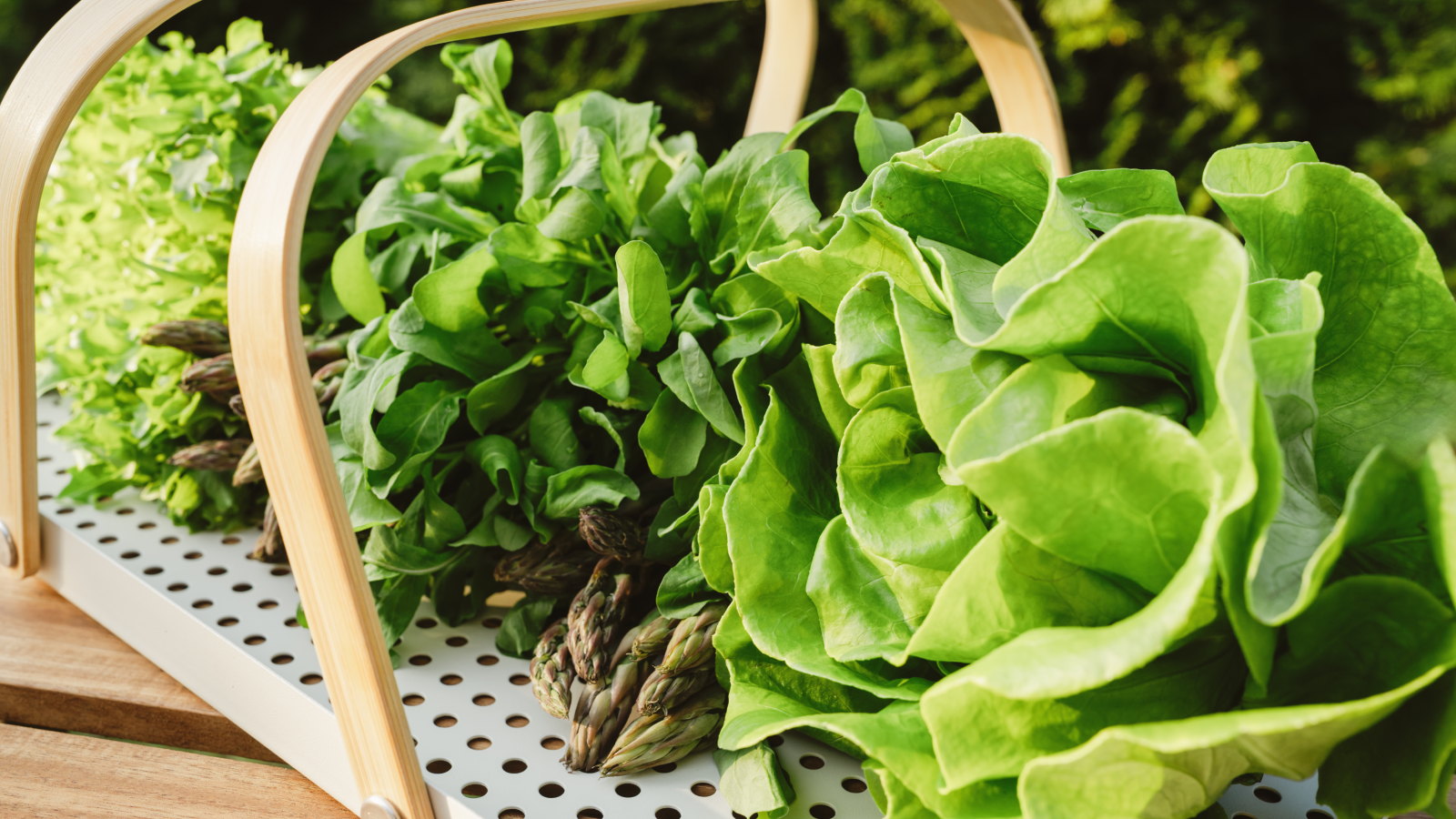 Lettuce, rocket, and other leafy greens lay on a wooden tray