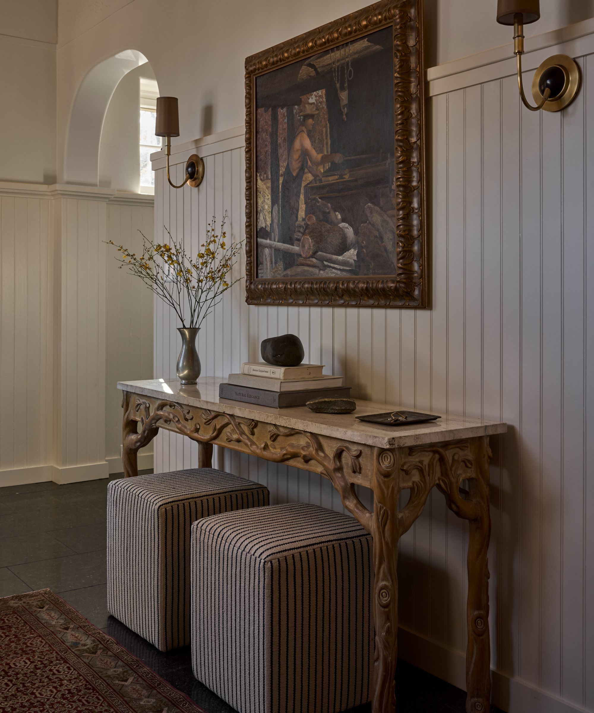 White paneled entryway with large vintage print and wooden carved console table