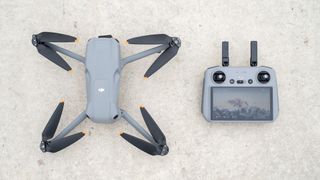 The DJI Air 3 sits on the ground with propellers open next to its controller.