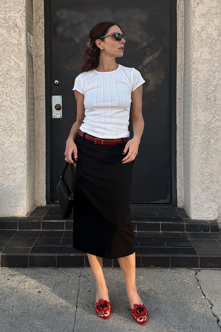 a woman wearing a white tee, black skort, red sandals, and red belt