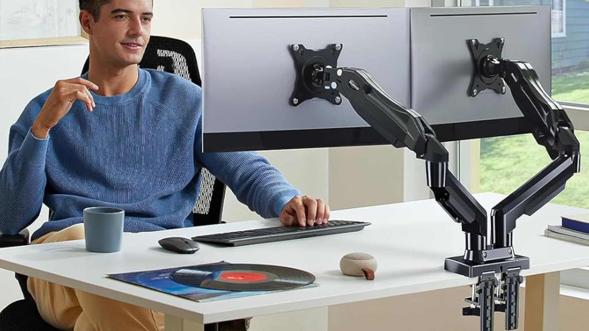A promotional image showing a person sat at a computer desk, using a Huanuo HNDS6 dual monitor arm