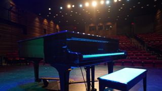 A piano shines on stage at Ontario venue with spotlights behind it. 