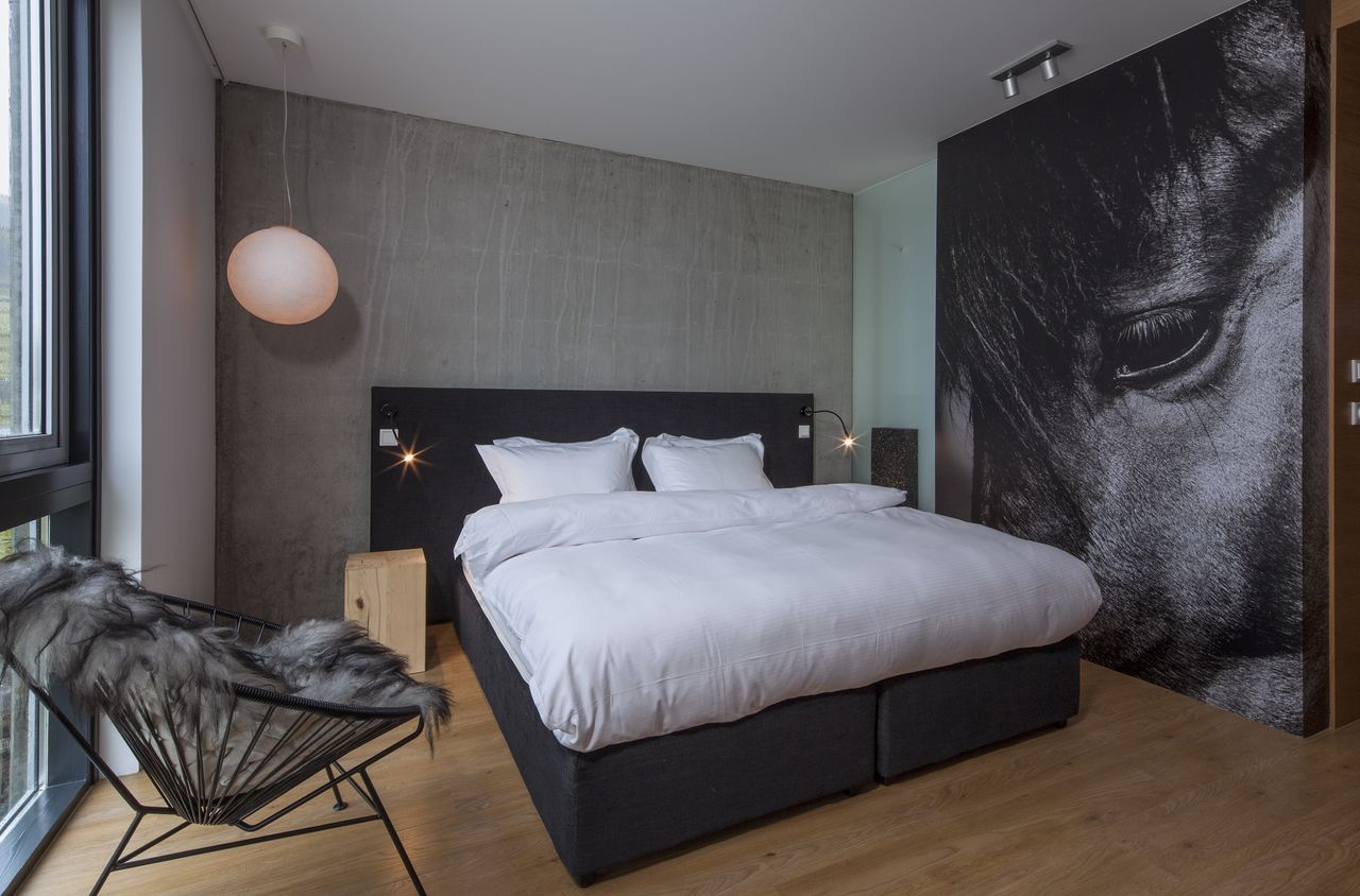 A hotel is nestled atop rocky formations in an Icelandic desert landscape, with floor-to-ceiling windows and minimal furnishings letting the outdoors in.