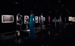 Dark room at the Mademoiselle Privé exhibition featuring black and white art on the wall and black mannequins displaying Karl Lagerfeld blue, red and darker coloured haute couture pieces and Coco Chanel jewellery
