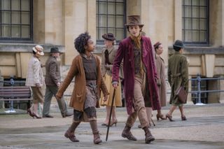 calah lane and timothee chalamet as willy wonka wearing a purple coat and hat walking through london in a still from wonka