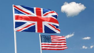 Flags of the United Kingdom and United States flying in the wind with a clear sky in background.