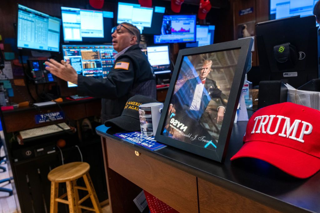 A picture of Donald Trump is displayed as traders work on the New York Stock Exchange (NYSE) floor alongside a red Trump hat