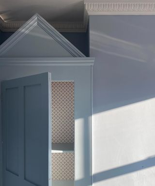 A color-drenched blue room with a cabinet built into the corner, topped with a cabinet hat