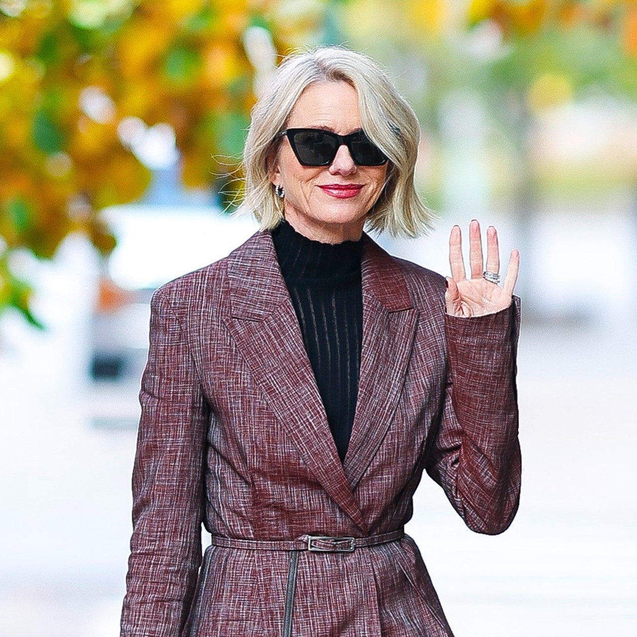 a paparazzi photo of a white woman with short blonde hair wearing a black turtleneck and a printed red coat