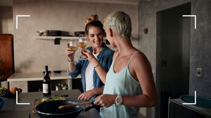 Two women cooking in a kitchen with glasses of white wine, after meeting on one of the best lesbian dating apps