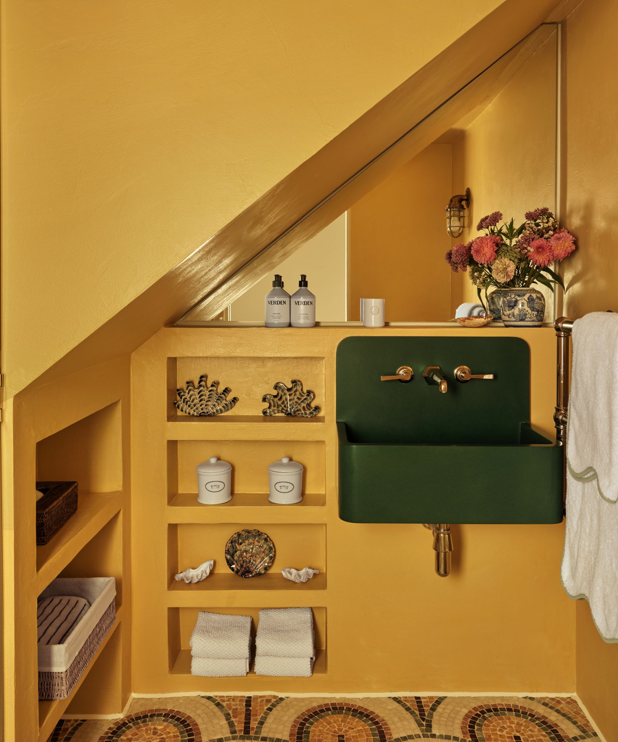 Bathroom with mosaic floor, yellow walls, sloped ceiling, open shelves, and green sink with gold faucet