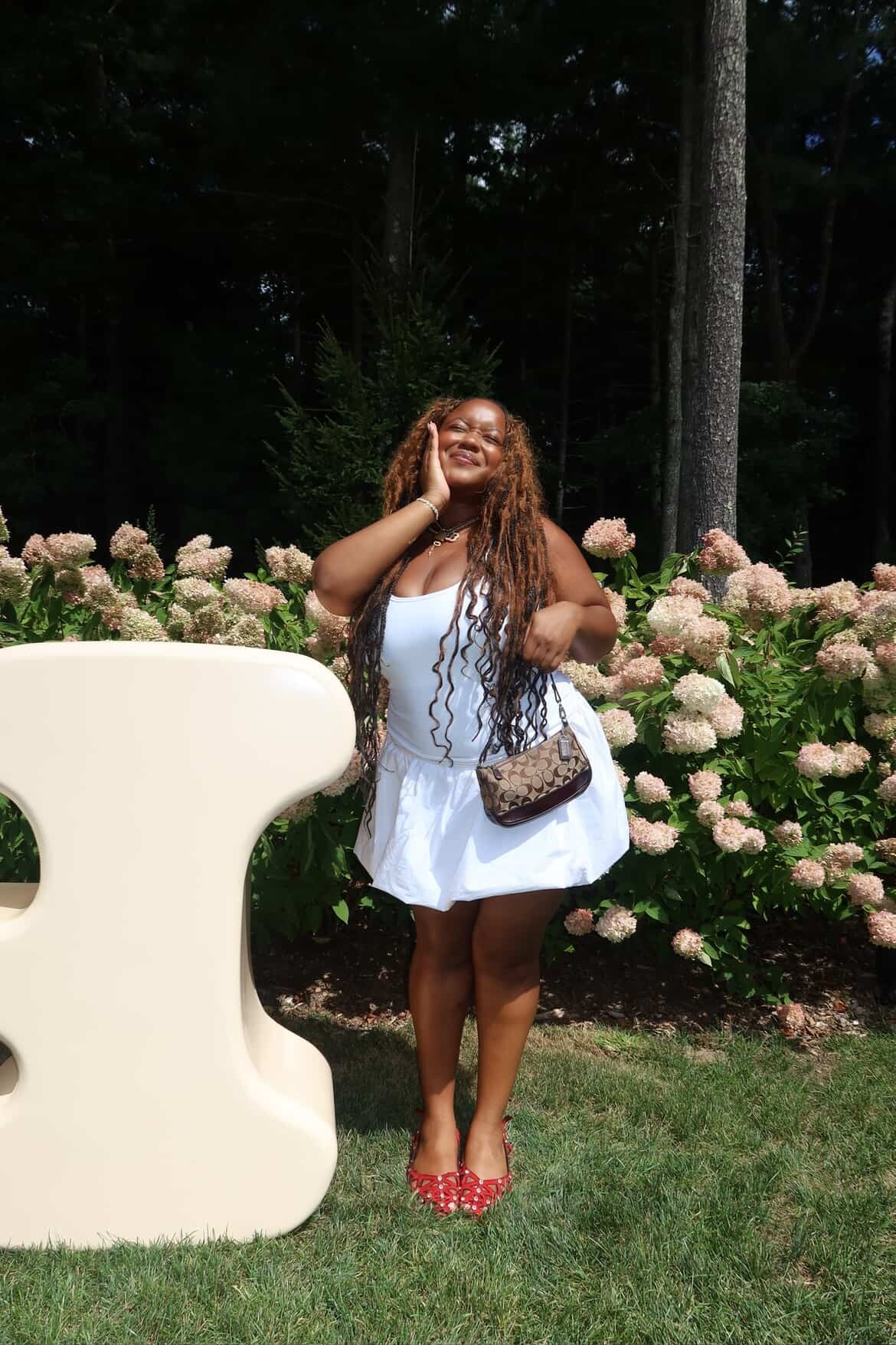 Ashlyn Delaney in a white dress, red shoes, carrying a brown Coach bag
