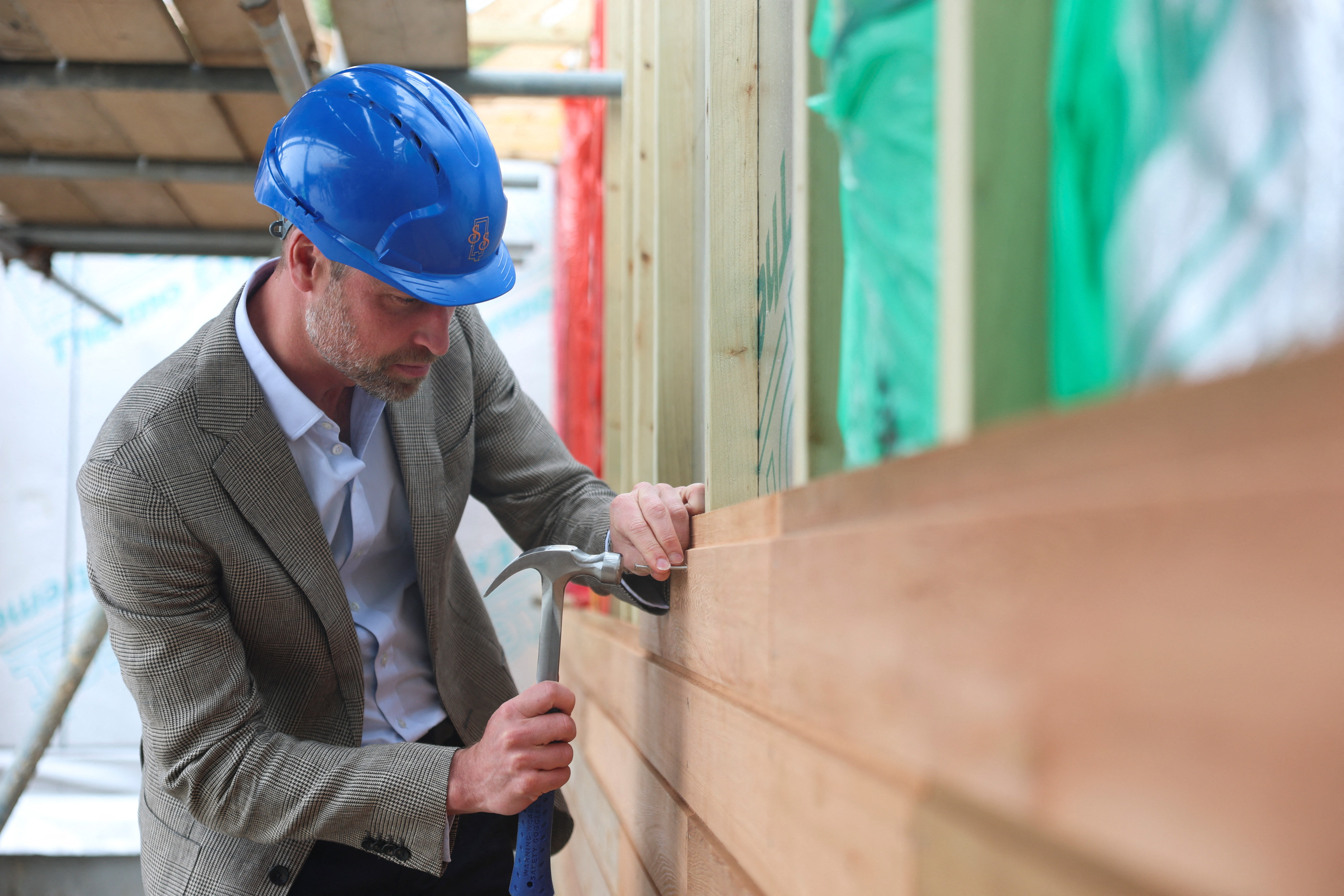 Prince William hammering a nail in a wall as he visits the construction site of 10 new sustainable homes delivered by the Duchy of Cornwall