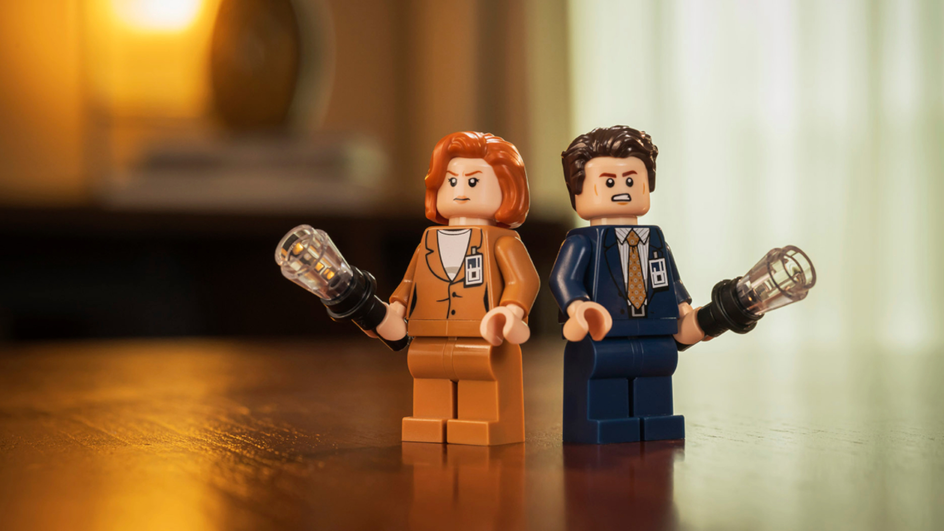Lego minifigures of Mulder and Scully holding flashlights, on a wooden table