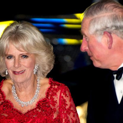 Queen Camilla wearing a red dress and diamonds next to King Charles in a tux
