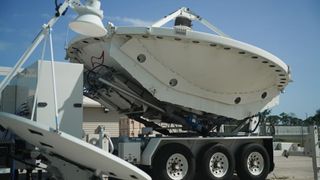 a large white radio antenna dish on the back of a truck bed, outside under a clear sky