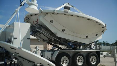 a large white radio antenna dish on the back of a truck bed, outside under a clear sky