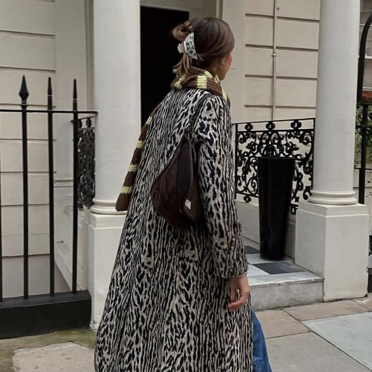Woman wears leopard print long coat, brown suede bag and striped scarf
