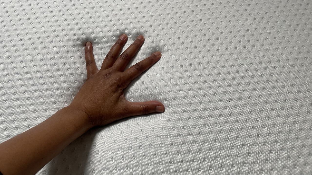 A hand touches the surface of the Emma Original mattress