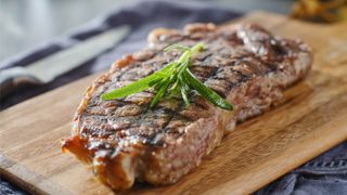 Cooked steak resting on a wooden board with a sprig of rosemary on top