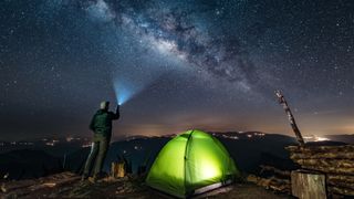 Man shining torch at stars outside illuminated tent