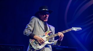 Steve Vai is suited and booted in grey and takes a solo on his Ibanez PIA onstage with Beat