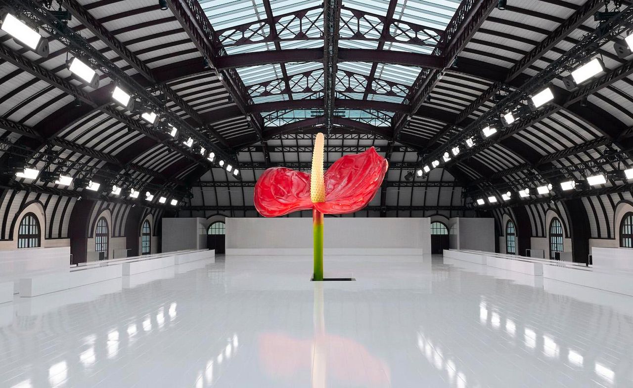 A large red anthurium flower stands in the middle of an all white show space inside a large exhibition room.