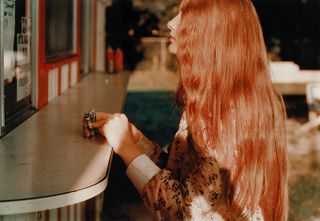 View of a girl with long red hair standing at a food truck holding money during the day