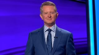 Ken Jennings wears a textured blue paisley tie over a patterned shirt and navy coat on Jeopardy.