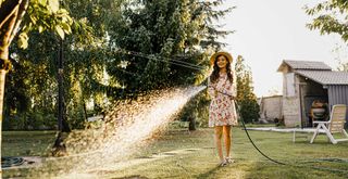woman watering a lawn early morning to avoid lawn care mistakes