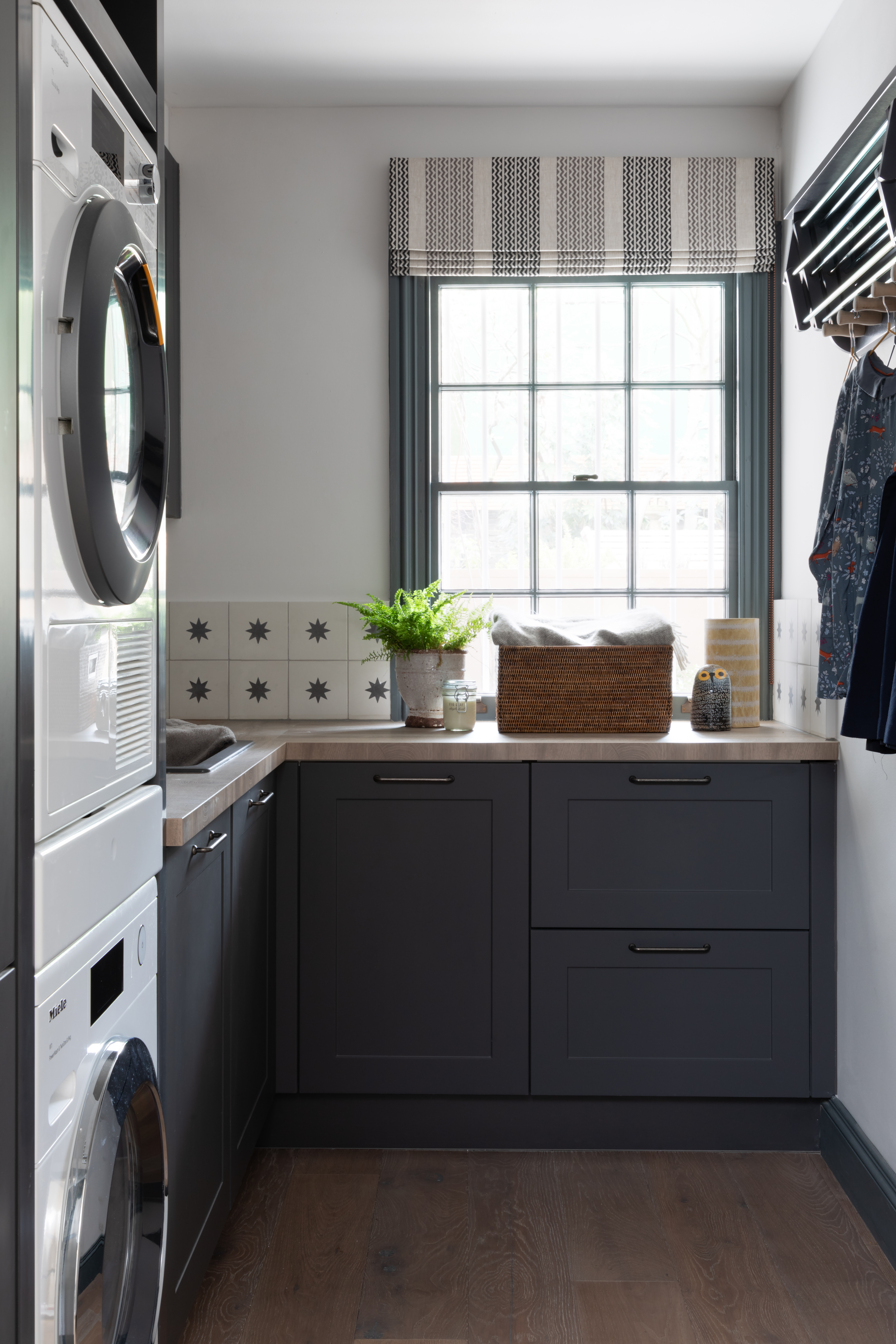 A utility room in shades of grey with motif tiles and washing appliances stacked on top of each other
