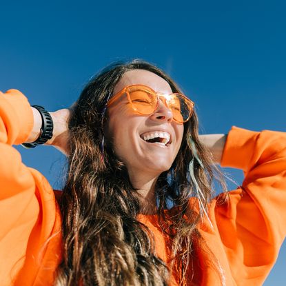 best vitamin c moisturisers - woman with glowy skin in bright orange jumper and sunglasses - getty 2181139566