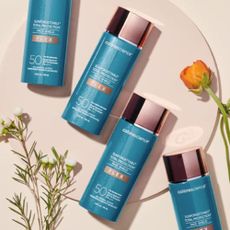 Four bottles of Colorescience Sunforgettable Total Face Shield Flex with SPF 50 on pale background with orange and white flowers