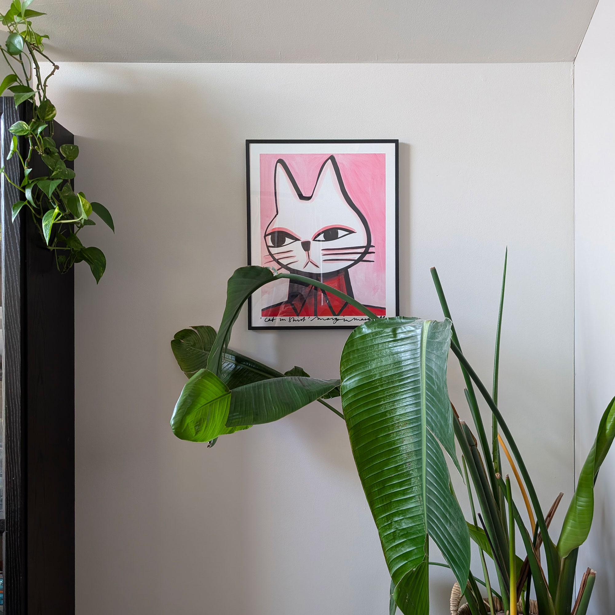 Painting of a white cat on wall behind large houseplant