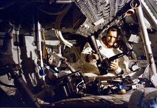 Richard F. Gordon attaches a high-resolution telephoto lens to a camera aboard the Apollo 12 Command Module Yankee Clipper.