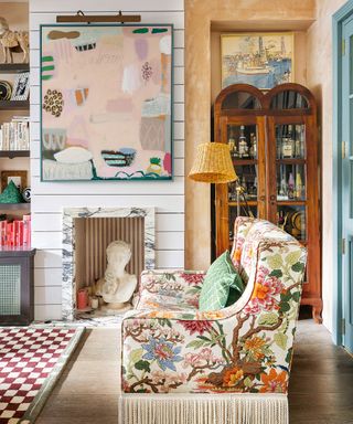 Colorful, maximalist living room with abstract artwork, floral upholstered sofa, antique shelving unit, checkered rug