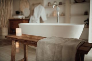 A white, free-standing bath, with a wooden stool next to it with a grey towel on.