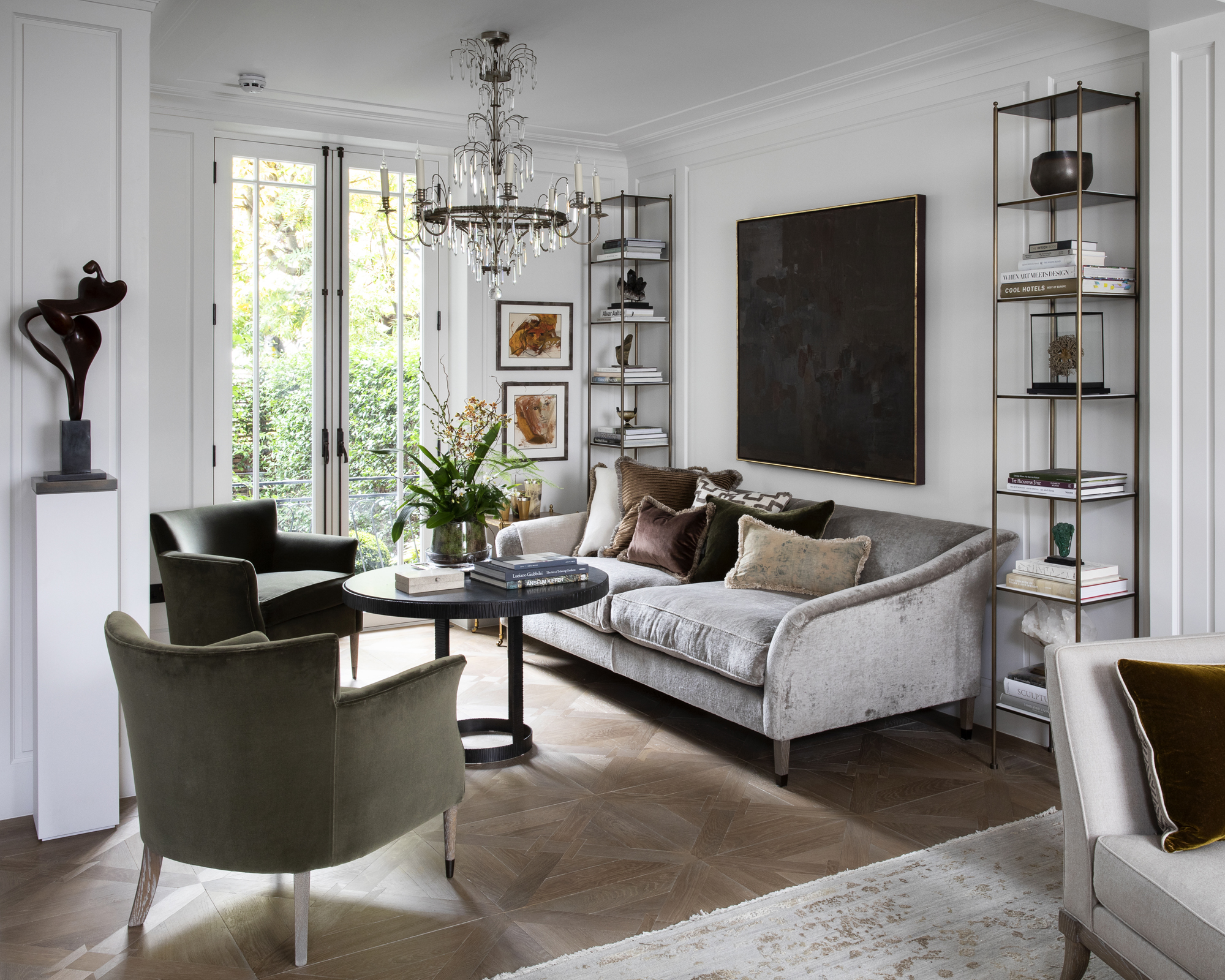 A living room with grey velvet sofa, white walls and dark green armchair