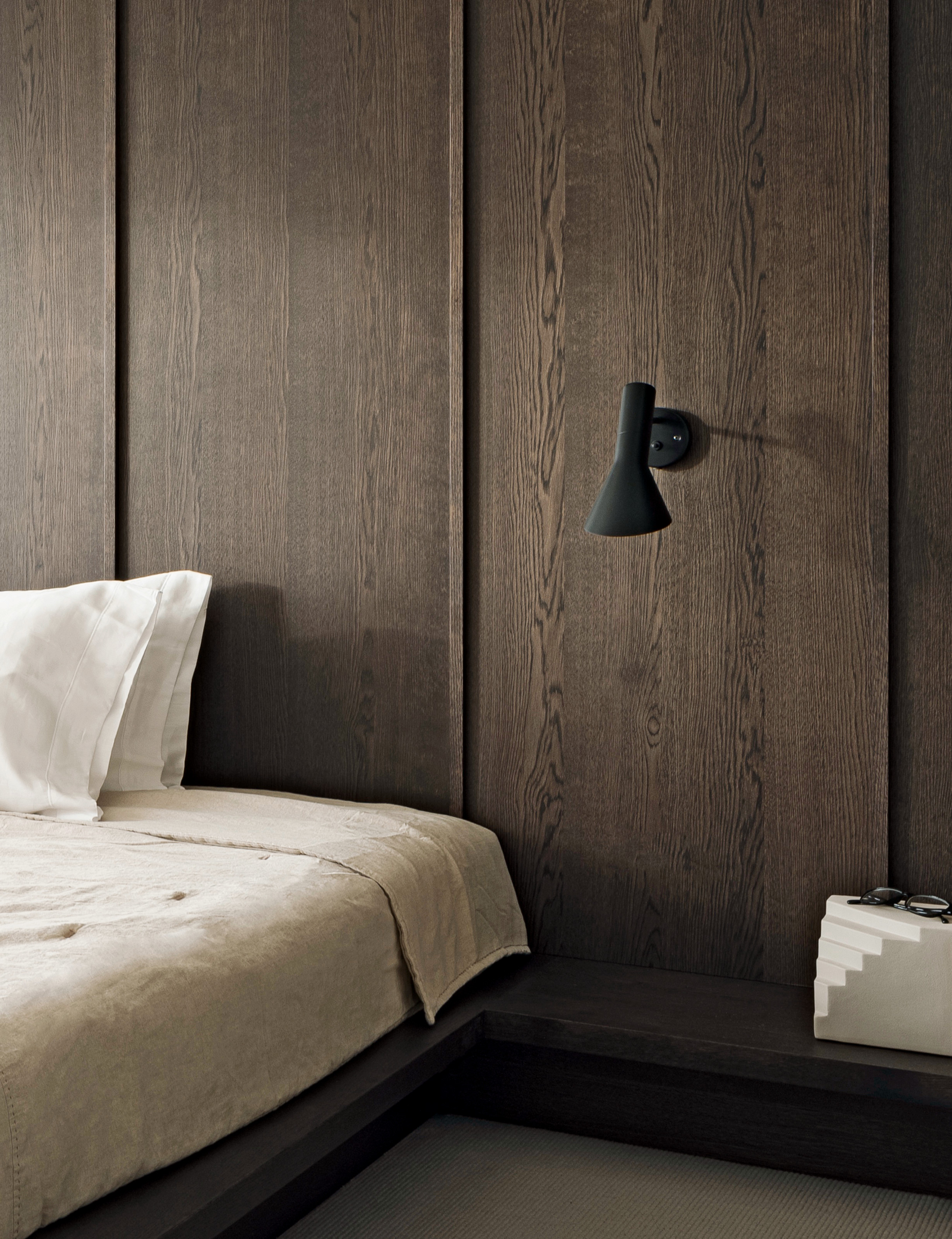 Bed on dark wood platform against wall paneling